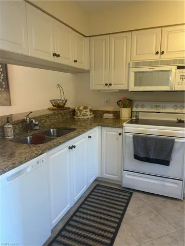 Kitchen with white range oven, white cabinetry, dishwashing machine, dark granite countertops, and light tile patterned floors