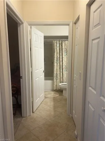 Hall closets and guest bathroom with shower / bath combo with shower curtain and light tile patterned floors