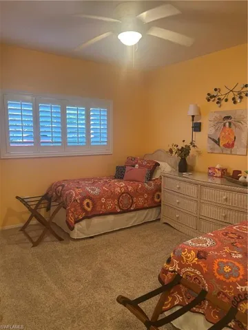 Guest bedroom is carpeted and has a ceiling fan and large window with plantation shutters.