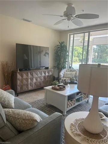 Living area with ceiling fan, tile patterned floors and large screen TV.