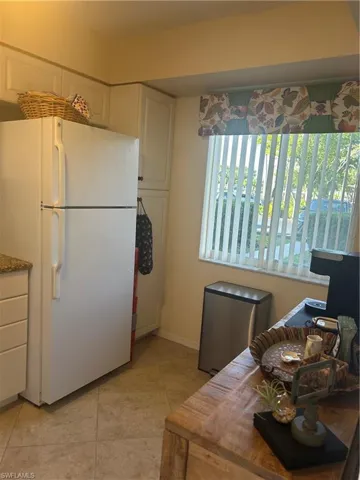 Kitchen featuring fridge, white cabinets, tile on the diagonal, and a larger window.