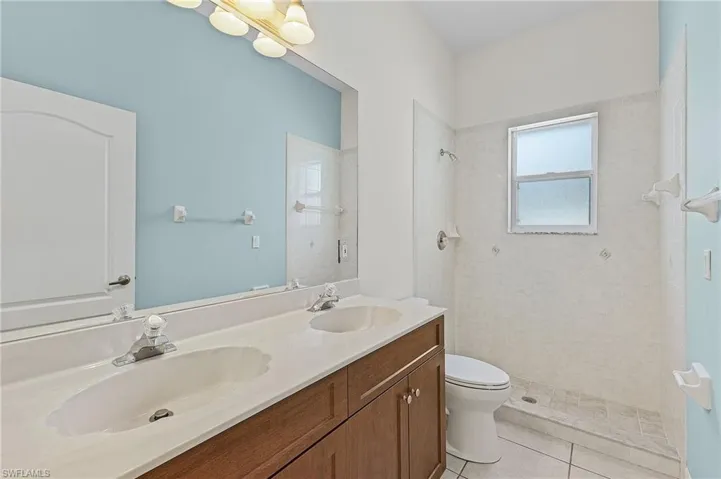 Bathroom featuring tile patterned floors, double sink vanity, a tile shower, and toilet