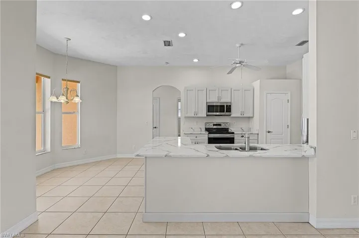 Kitchen with stainless steel appliances, sink, white cabinets, light tile patterned flooring, and hanging light fixtures