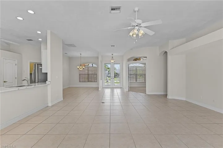 Unfurnished living room featuring sink, french doors, ceiling fan with notable chandelier, and light tile patterned floors