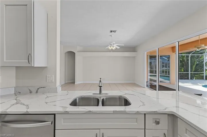 Kitchen with ceiling fan, stainless steel dishwasher, white cabinets, light stone countertops, and sink