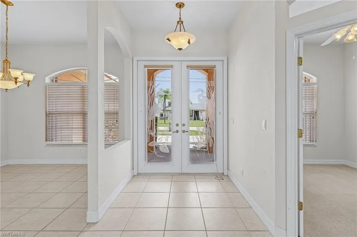 Foyer featuring light tile patterned floors, a chandelier, french doors, and a healthy amount of sunlight