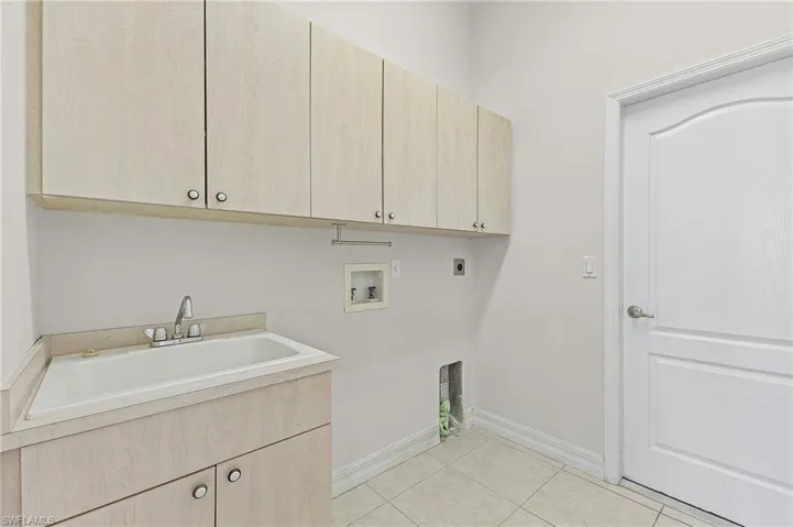 Laundry area featuring sink, electric dryer hookup, washer hookup, cabinets, and light tile patterned floors