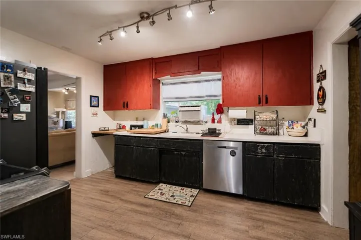 Kitchen featuring wood-finish flooring, a stainless steel dishwasher, track lighting, a window over the sink, and a combination of red and black cabinetry