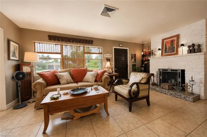 Spacious living area featuring neutral-toned tile flooring, a white brick fireplace with a stone hearth, and multiple windows