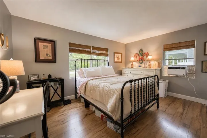 Spacious room featuring wood-finish flooring, two windows with woven shades, and a window-mounted AC unit