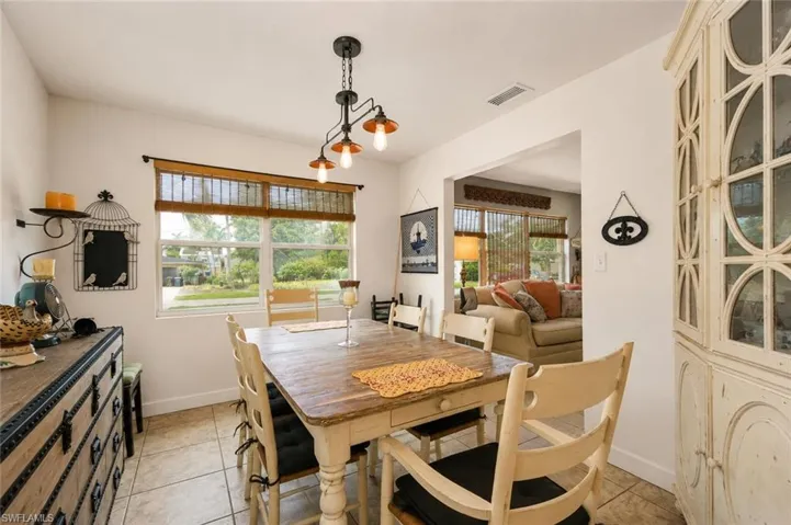 Dining area featuring a rustic wood-finish table, tile flooring, a multi-bulb chandelier, and a wide window with woven wood blinds