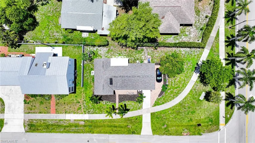 Aerial view showcasing the property with a shingled roof, paver driveway, and mature landscaping