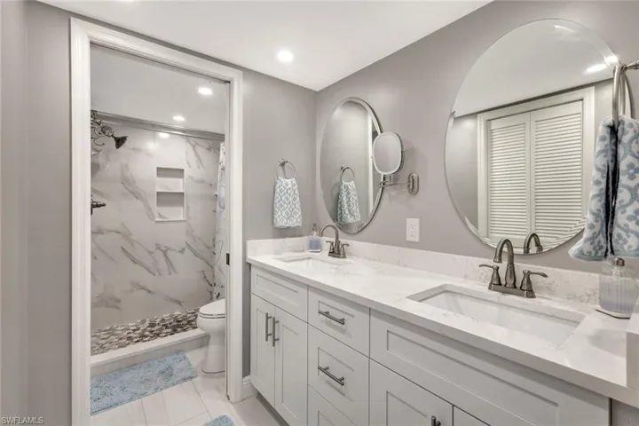 Bathroom with curtained shower, dual bowl vanity, toilet, and tile floors
