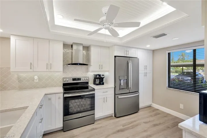 Kitchen with wall chimney range hood, light hardwood / wood-style floors, a tray ceiling, and appliances with stainless steel finishes