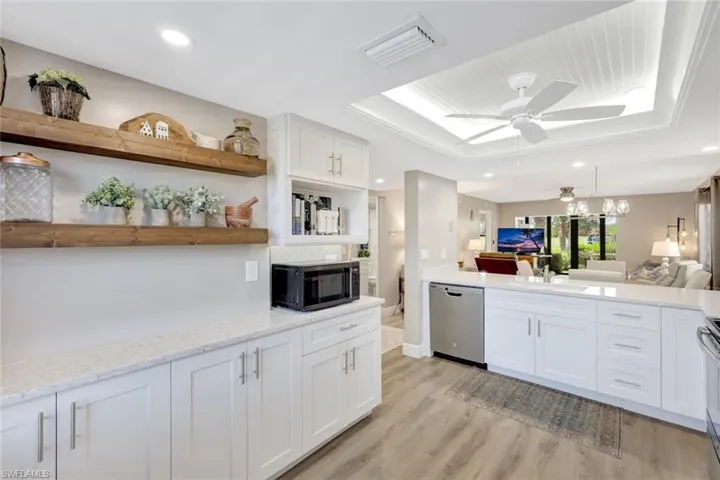 Kitchen featuring light hardwood / wood-style floors, ceiling fan with notable chandelier, a tray ceiling, white cabinets, and appliances with stainless steel finishes