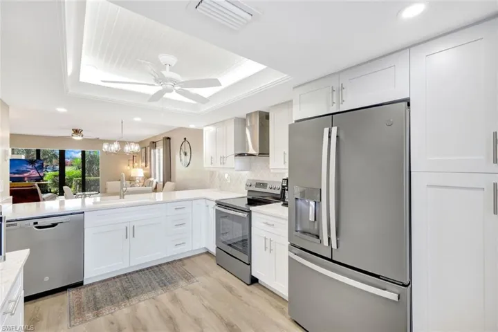 Kitchen with wall chimney range hood, ceiling fan with notable chandelier, light hardwood / wood-style flooring, and appliances with stainless steel finishes