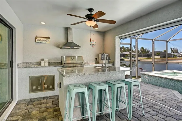 Full Outdoor Kitchen featuring light stone countertops, ceiling fan, and an island with sink and ice machine/refrigerator