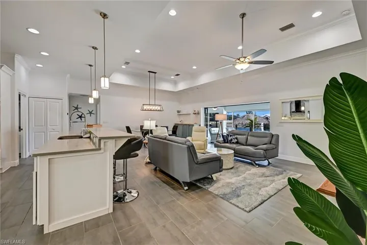 Living room featuring crown molding, a ceiling fan, tiled floors, a tray ceiling, and recessed lighting.