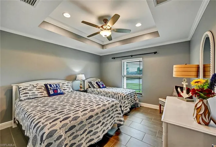 Bedroom with crown molding, a ceiling fan, a tray ceiling, tile floors, and recessed lighting.