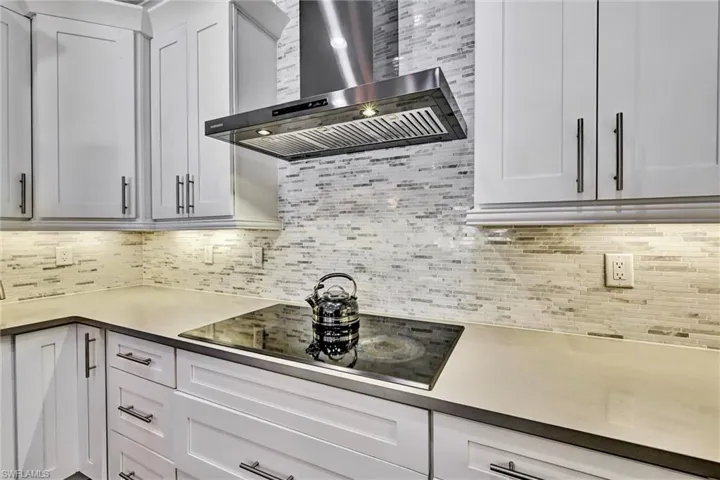Kitchen with under-cabinet LED lighting, black electric stovetop, and light countertops