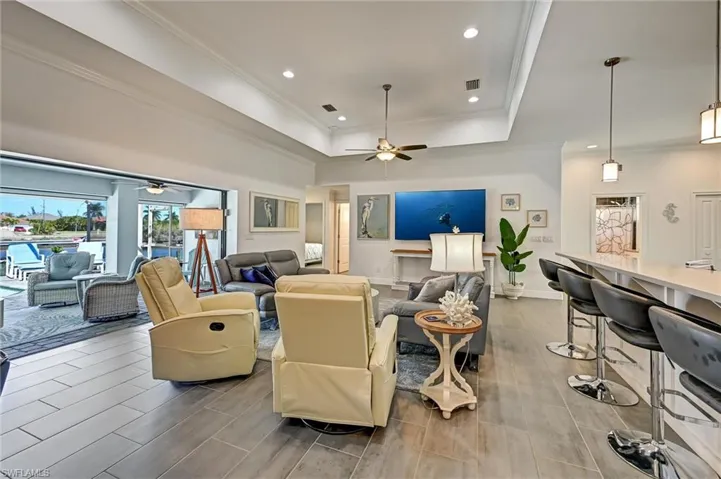 Living room featuring crown molding, a ceiling fan, tiled floors, a tray ceiling, and recessed lighting.