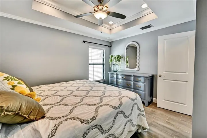 Bedroom with crown molding, a ceiling fan, a tray ceiling, tile floors, and recessed lighting.