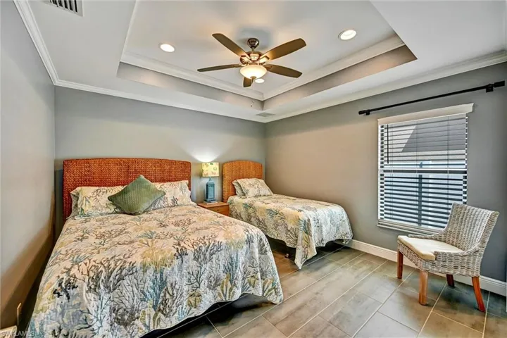Bedroom with crown molding, a ceiling fan, a tray ceiling, tile floors, and recessed lighting.