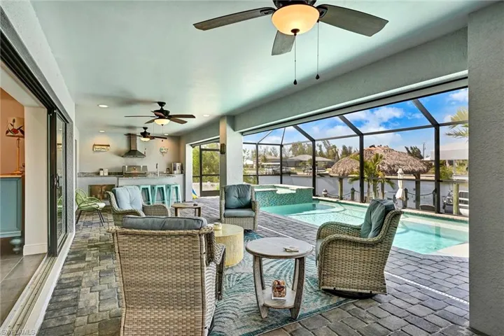 View of patio featuring a sunroom, ceiling fan, a pool with a connected hot tub, and an outdoor bar and grill - game day ready