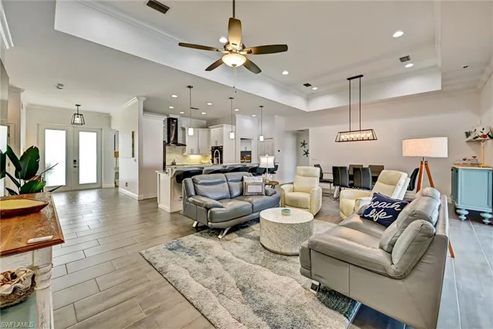 Living room featuring crown molding, a ceiling fan, tiled floors, a tray ceiling, and recessed lighting.