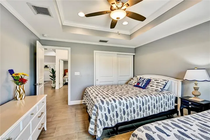 Bedroom with crown molding, a ceiling fan, a tray ceiling, tile floors, and recessed lighting.