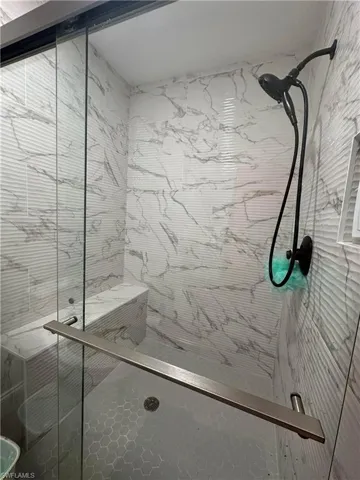 Glass-enclosed shower featuring a built-in bench, hexagonal floor tiles, and a matte black shower fixture