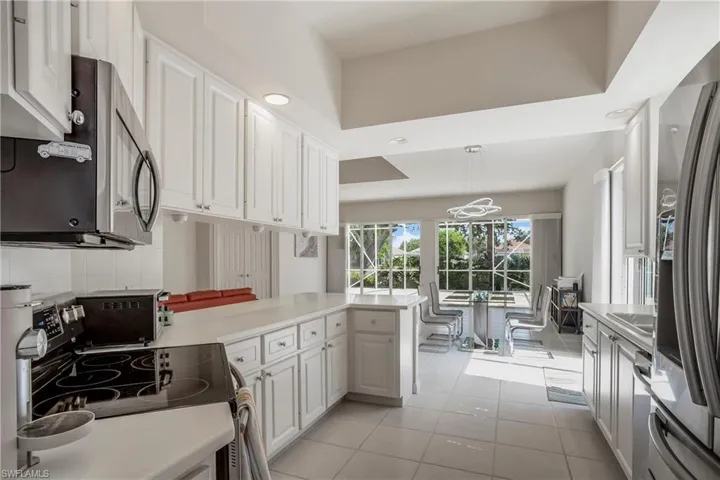 Kitchen featuring light tile patterned flooring, light countertops, tasteful backsplash, stainless steel appliances, and white cabinets