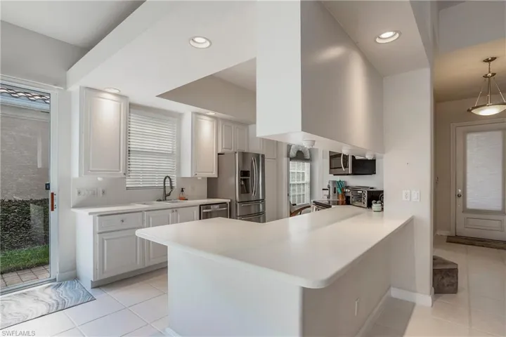 Kitchen featuring light countertops, light tile patterned floors, a sink, a peninsula, and appliances with stainless steel finishes