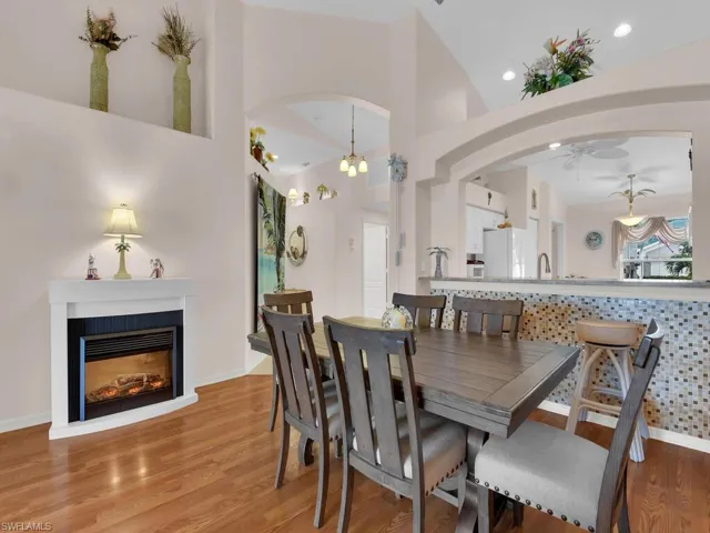 Dining space with arched walkways, wood finished floors, ceiling fan, a glass covered fireplace, and a towering ceiling