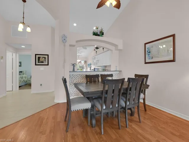 Dining space featuring a ceiling fan, arched walkways, wood finished floors, high vaulted ceiling, and a chandelier
