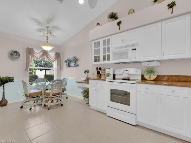 Kitchen featuring white appliances, lofted ceiling, white cabinetry, glass insert cabinets, and light tile patterned flooring