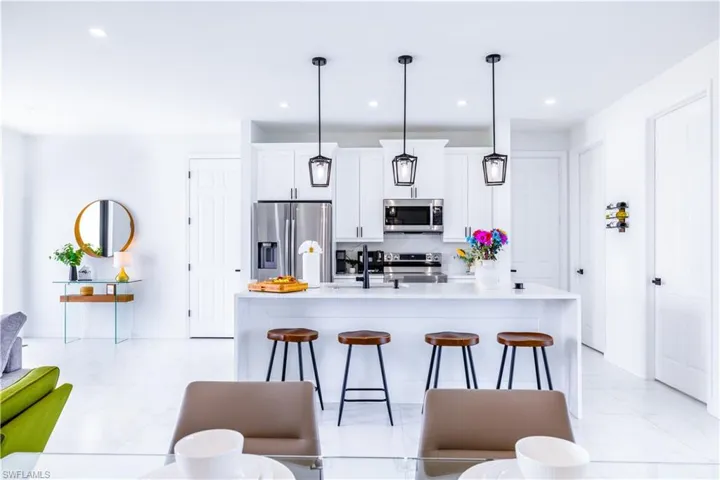 Kitchen with appliances with stainless steel finishes, white cabinetry, a breakfast bar area, light stone countertops, and decorative light fixtures