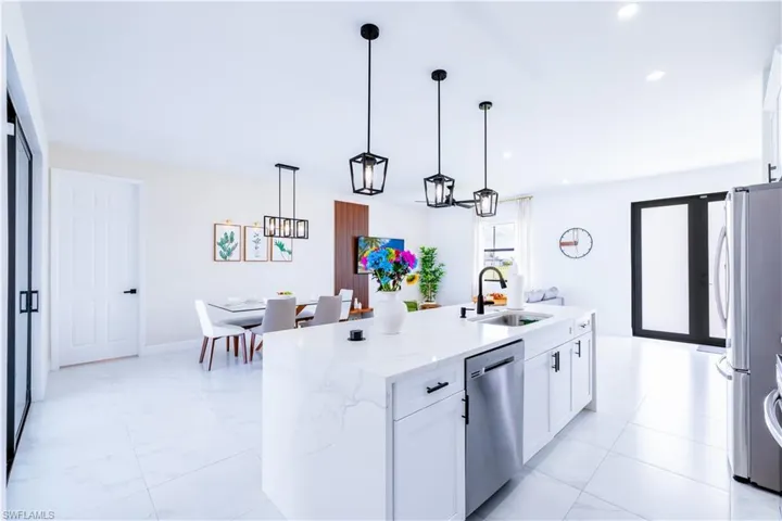 Kitchen featuring white cabinetry, pendant lighting, light stone countertops, stainless steel appliances, and a kitchen island with sink