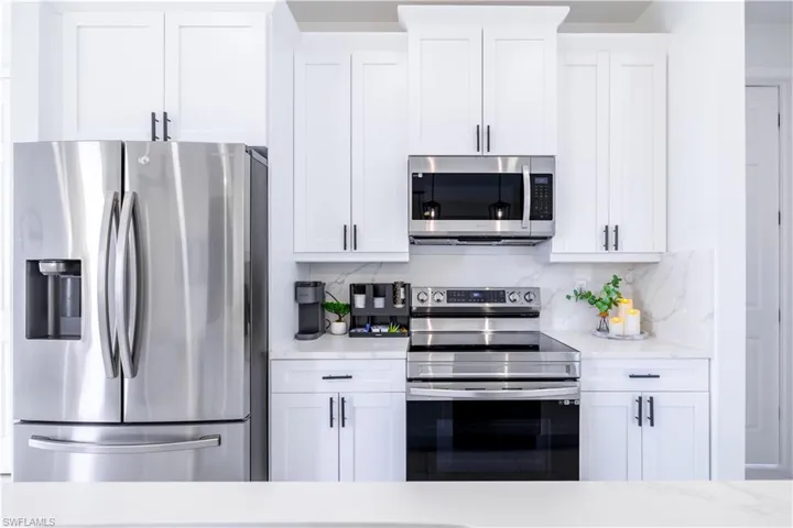Kitchen featuring appliances with stainless steel finishes, white cabinetry, tasteful backsplash, and light stone countertops