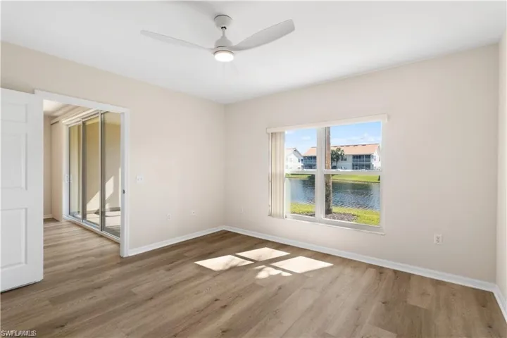 Empty room with a water view, wood finished floors, and a ceiling fan