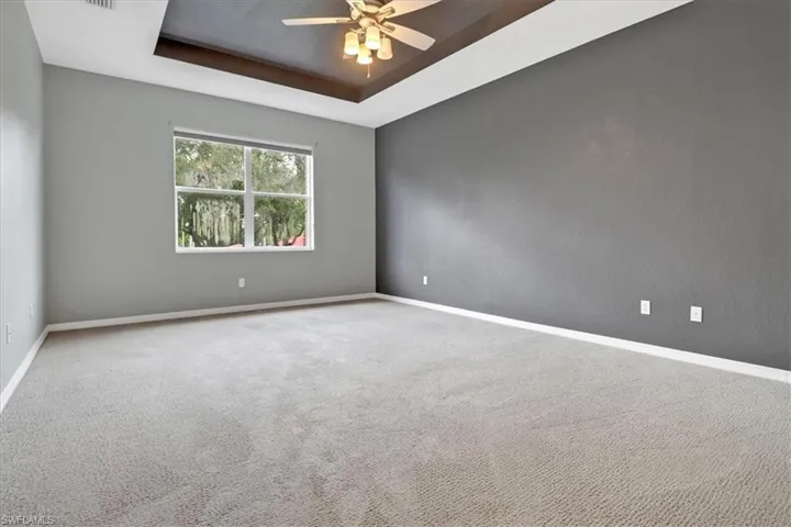Carpeted empty room with ceiling fan and a raised ceiling