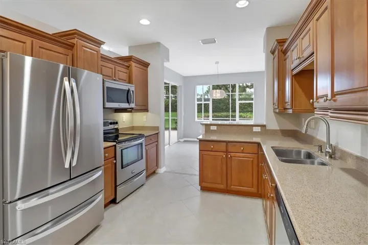 Kitchen featuring stainless steel appliances, sink, decorative light fixtures, light stone countertops, and light tile patterned flooring