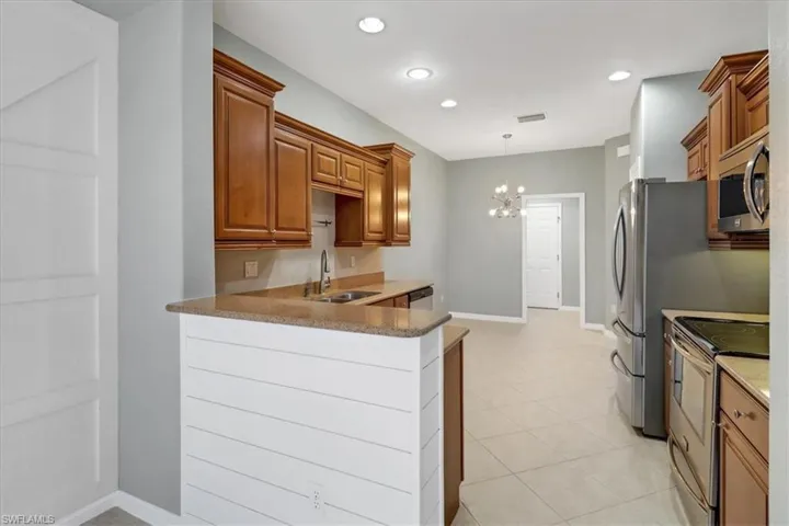 Kitchen featuring light tile patterned floors, kitchen peninsula, appliances with stainless steel finishes, decorative light fixtures, and sink