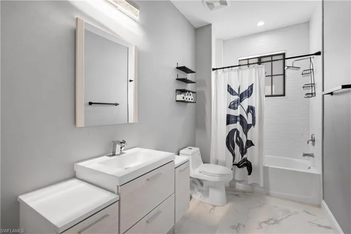 Bathroom featuring a modern vanity with integrated sink, white marble-look flooring, built-in bathtub, and horizontal white tile wall surround
