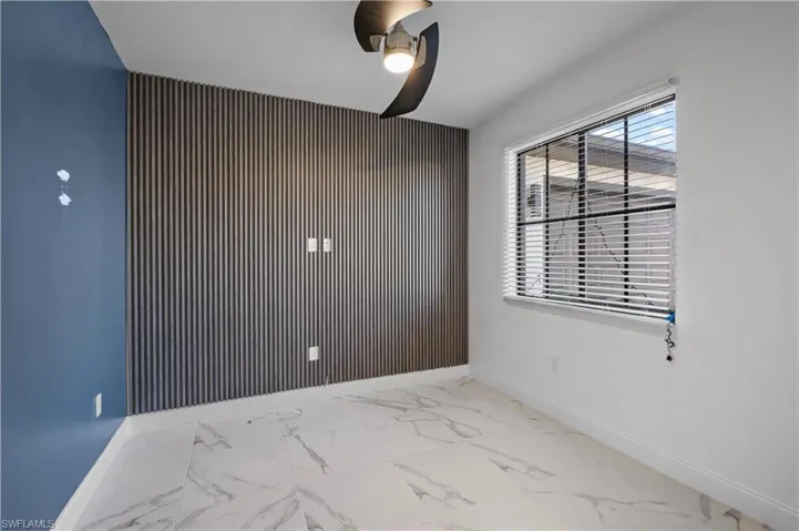 Accent wall with vertical paneling, large window with blinds, ceiling fan, and white baseboards