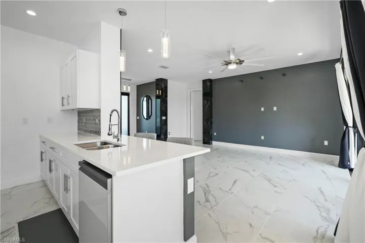 Open-concept living space featuring a kitchen island with a double basin sink, white shaker cabinetry, quartz countertops, and a patterned tile backsplash