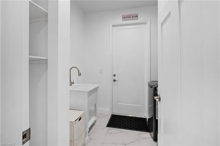 Laundry room featuring a white utility sink with a gooseneck faucet, marble-look floor tiles, and a built-in shelving unit