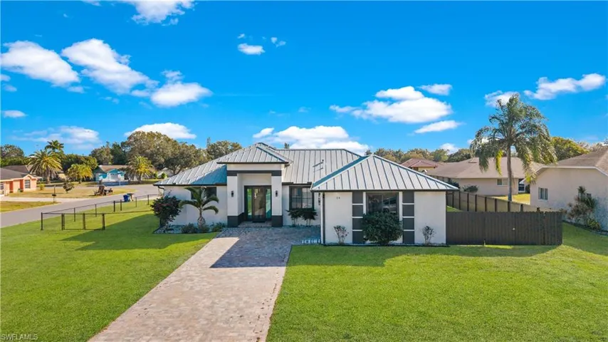 Contemporary-style residence featuring a prominent metal roof, a paver driveway, and a manicured lawn