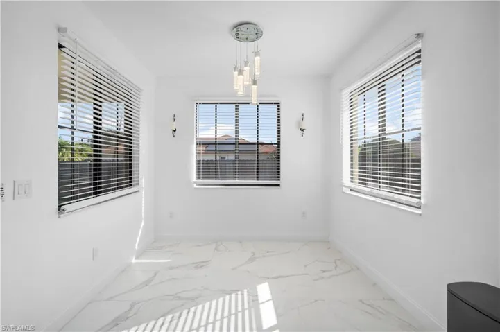 Bright room featuring white walls, large windows with horizontal blinds, and a contemporary chandelier