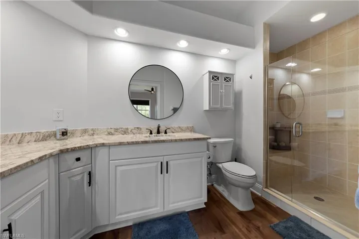 Bathroom featuring a shower with frameless door, granite vanity, toilet, and vinyl wood-style floors